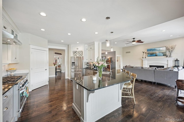 kitchen with stainless steel fridge, a breakfast bar, a kitchen island with sink, pendant lighting, and white cabinets