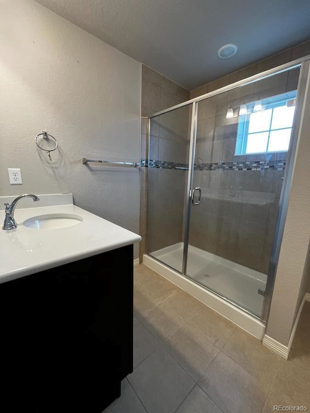 full bath featuring baseboards, a stall shower, vanity, and tile patterned flooring