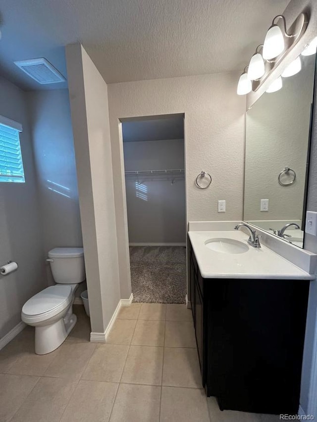 bathroom featuring vanity, visible vents, tile patterned flooring, a walk in closet, and toilet