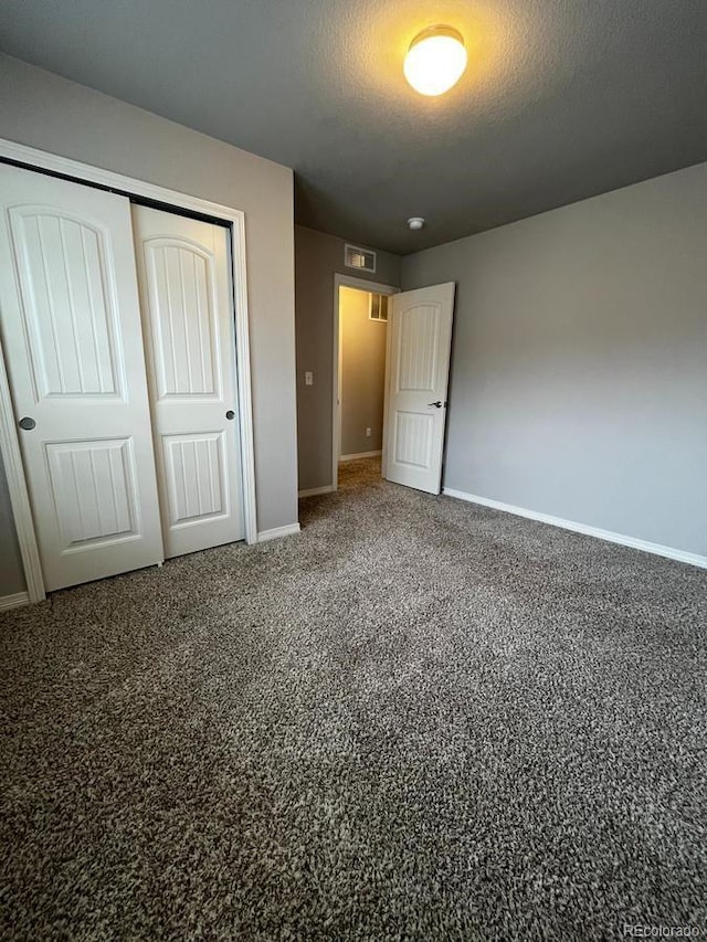 unfurnished bedroom featuring visible vents, baseboards, a closet, a textured ceiling, and carpet flooring