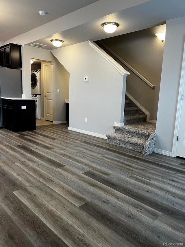 unfurnished living room with stairway, dark wood-style floors, baseboards, and stacked washing maching and dryer