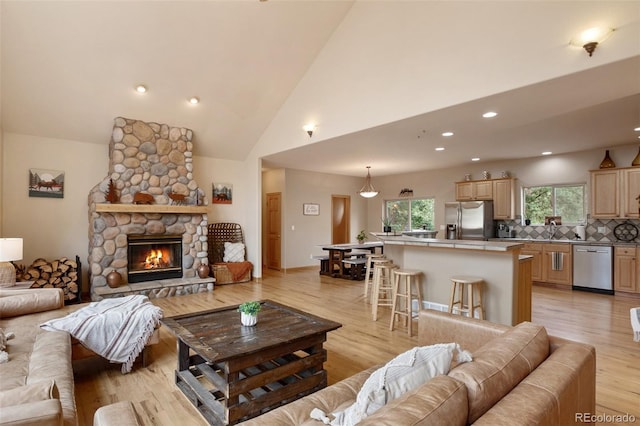 living room with plenty of natural light, high vaulted ceiling, a fireplace, and light hardwood / wood-style flooring