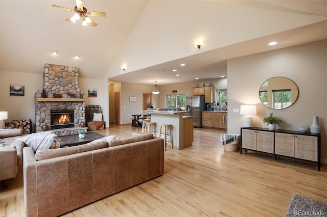 living room featuring ceiling fan, high vaulted ceiling, a fireplace, and light wood-type flooring