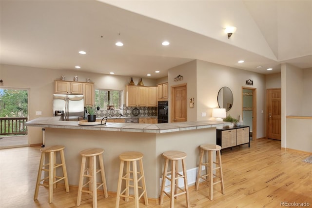 kitchen featuring tile counters, a breakfast bar, stainless steel fridge with ice dispenser, and light brown cabinetry