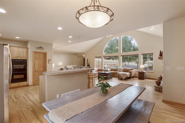 dining space with high vaulted ceiling and light hardwood / wood-style floors