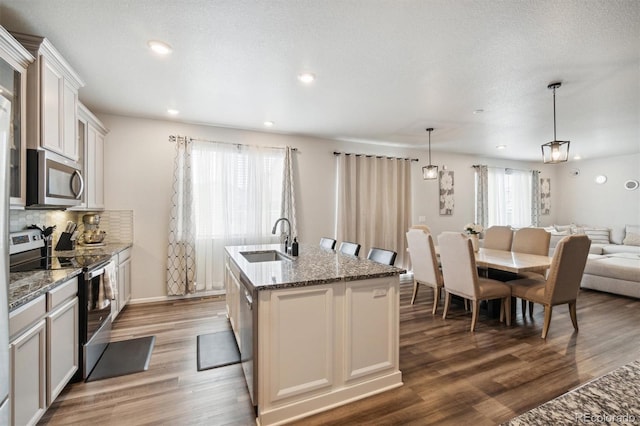 kitchen with a center island with sink, hanging light fixtures, appliances with stainless steel finishes, and a wealth of natural light