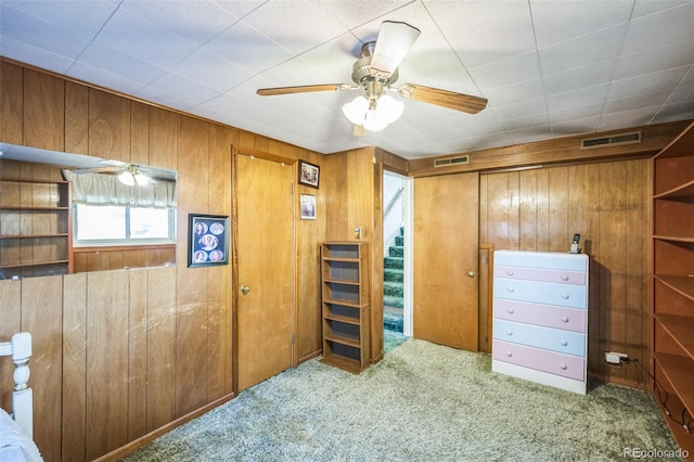 unfurnished bedroom with wooden walls, light colored carpet, a closet, and ceiling fan