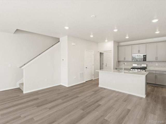 kitchen with appliances with stainless steel finishes, sink, gray cabinetry, a kitchen island with sink, and light hardwood / wood-style floors