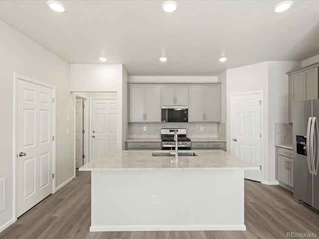 kitchen with light stone counters, sink, a center island with sink, and appliances with stainless steel finishes