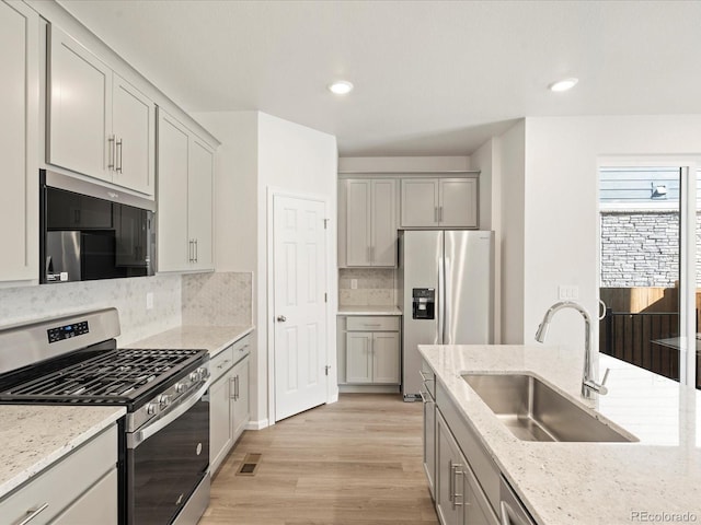 kitchen with sink, backsplash, light stone counters, stainless steel appliances, and light hardwood / wood-style flooring