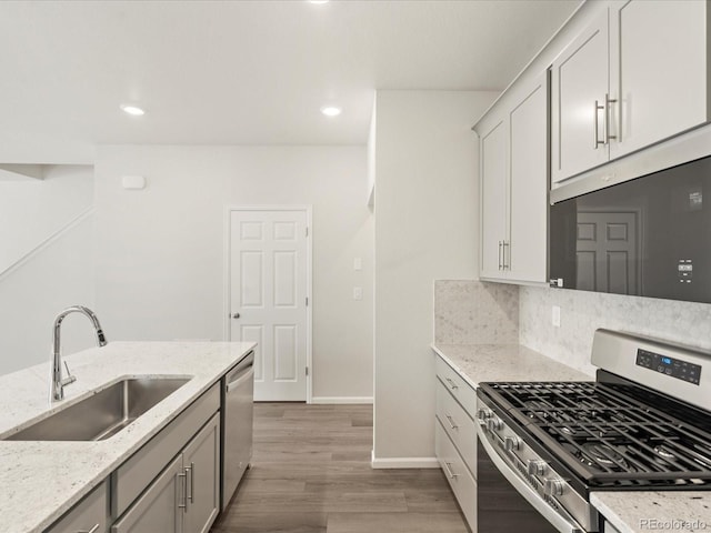 kitchen with sink, decorative backsplash, light hardwood / wood-style floors, light stone counters, and stainless steel appliances