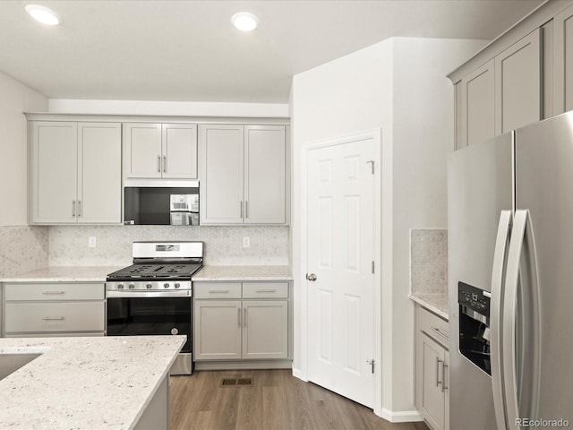 kitchen featuring tasteful backsplash, light stone countertops, appliances with stainless steel finishes, and gray cabinets