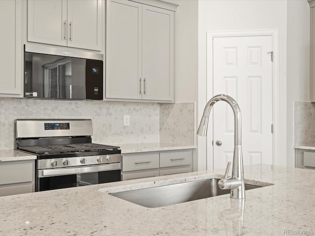 kitchen featuring sink, gray cabinetry, light stone counters, stainless steel gas range oven, and backsplash