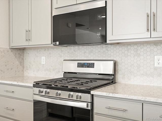 kitchen with light stone counters, backsplash, gas range, and white cabinets