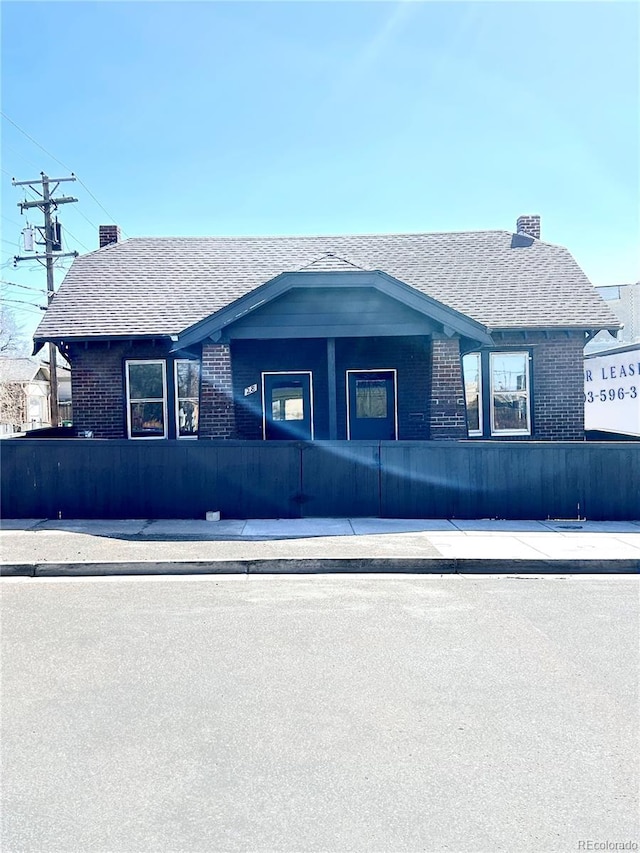 view of front facade with brick siding, a chimney, and roof with shingles