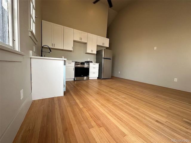 kitchen with light wood finished floors, light countertops, stainless steel appliances, white cabinets, and high vaulted ceiling