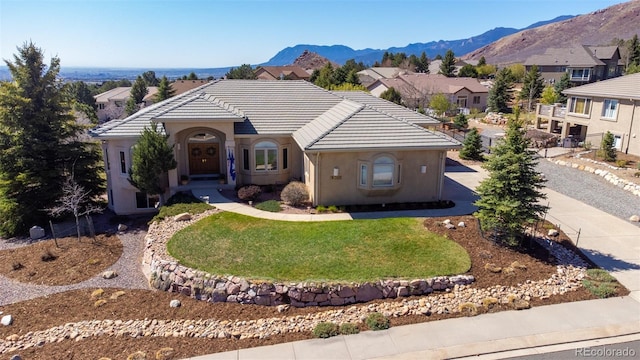 6240 Wilson Rd, Colorado Springs, CO 80919 - view of front of house with concrete driveway, a mountain view, a tiled roof, a front yard, and stucco siding