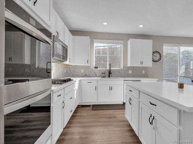 kitchen featuring tasteful backsplash, sink, white cabinets, stainless steel appliances, and light hardwood / wood-style flooring