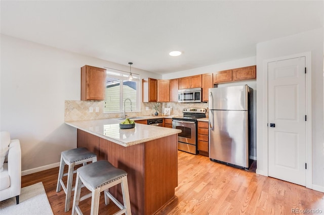 kitchen featuring appliances with stainless steel finishes, pendant lighting, sink, kitchen peninsula, and light wood-type flooring