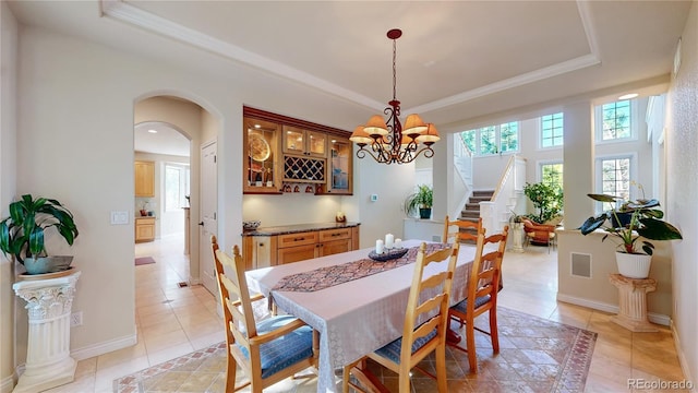 dining area with light tile patterned floors, a raised ceiling, arched walkways, a chandelier, and stairs