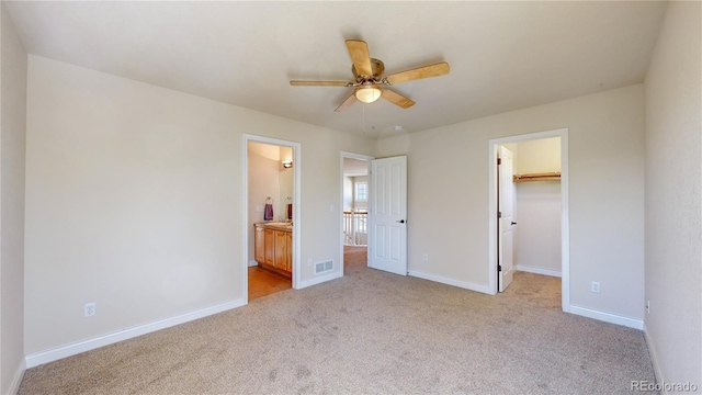 unfurnished bedroom featuring baseboards, light carpet, connected bathroom, a walk in closet, and visible vents