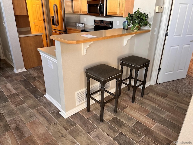 kitchen featuring a peninsula, a breakfast bar, wood finish floors, and appliances with stainless steel finishes