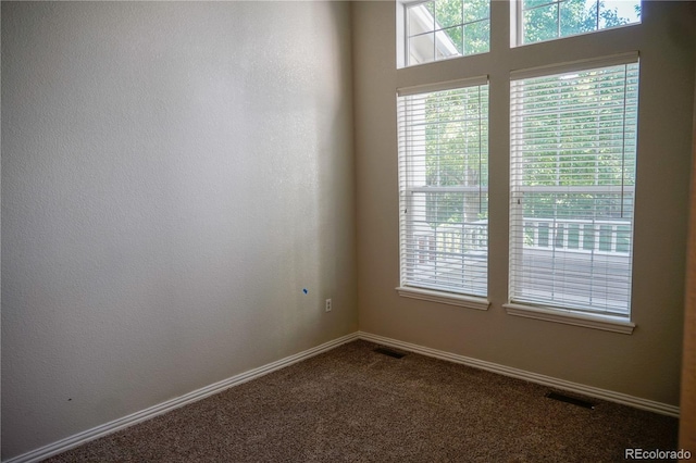 empty room featuring dark colored carpet, visible vents, and baseboards