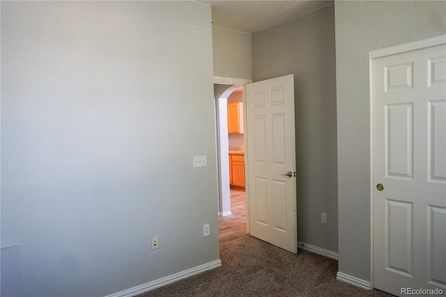 unfurnished bedroom featuring dark colored carpet, arched walkways, and baseboards