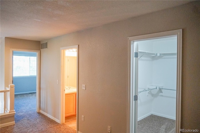corridor with visible vents, baseboards, a sink, a textured ceiling, and light carpet