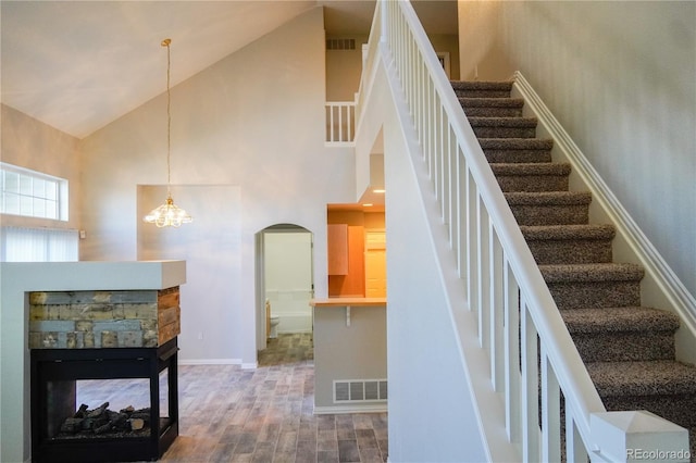 stairway featuring arched walkways, wood finished floors, high vaulted ceiling, and visible vents