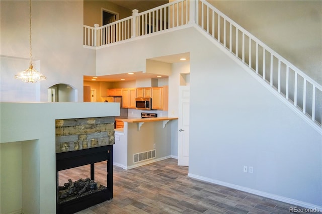 kitchen with stainless steel microwave, dark wood-style flooring, a breakfast bar, visible vents, and light brown cabinetry