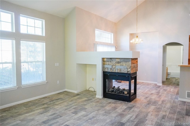 living room with arched walkways, wood finished floors, and high vaulted ceiling