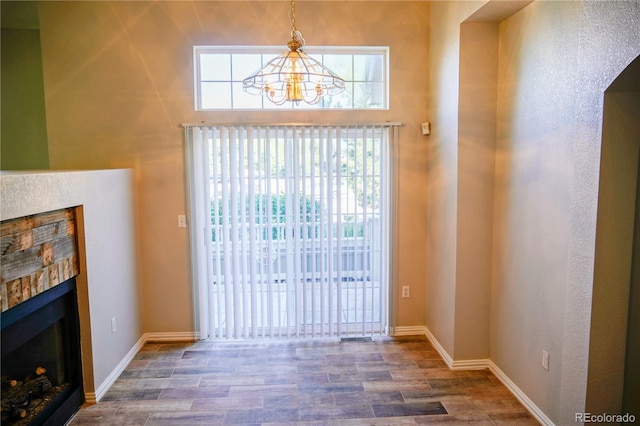 interior space featuring baseboards, wood finished floors, a notable chandelier, and a glass covered fireplace