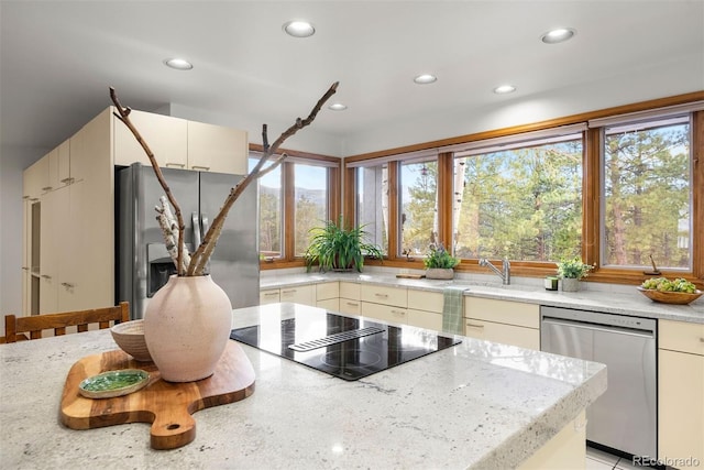 kitchen featuring stainless steel appliances, recessed lighting, cream cabinetry, and light stone counters