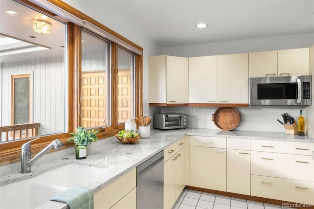 kitchen with cream cabinets, appliances with stainless steel finishes, backsplash, and a sink