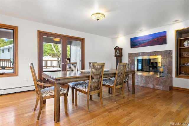 dining area with a baseboard radiator, light wood-style flooring, french doors, and a high end fireplace