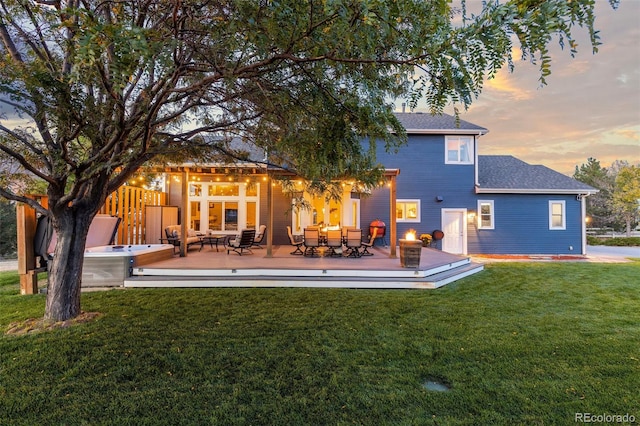 back of property at dusk with a yard, a wooden deck, and an outdoor hot tub