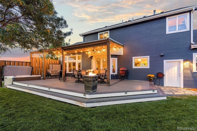 rear view of property with a fire pit, fence, a deck, and a lawn