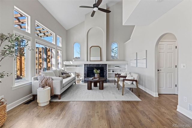 interior space featuring arched walkways, high vaulted ceiling, a premium fireplace, and wood finished floors