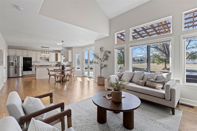 living room featuring light wood-style floors, baseboards, a high ceiling, and visible vents