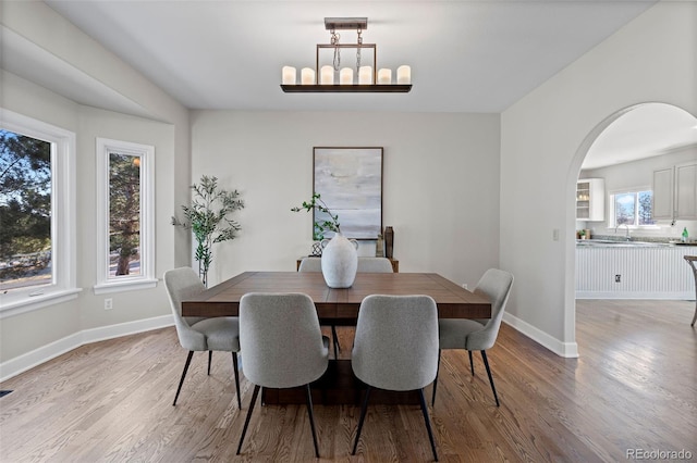 dining space with arched walkways, light wood-style flooring, and baseboards