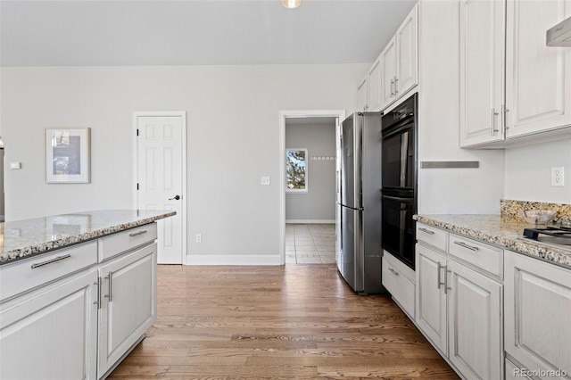 kitchen featuring dobule oven black, light stone counters, freestanding refrigerator, light wood-style floors, and white cabinetry