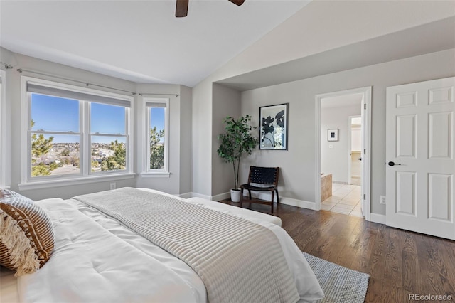 bedroom featuring a ceiling fan, vaulted ceiling, ensuite bath, wood finished floors, and baseboards