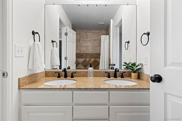 full bathroom featuring double vanity, tiled shower, and a sink