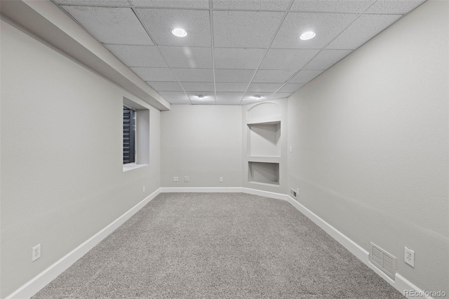 finished basement with baseboards, visible vents, a paneled ceiling, carpet floors, and built in shelves