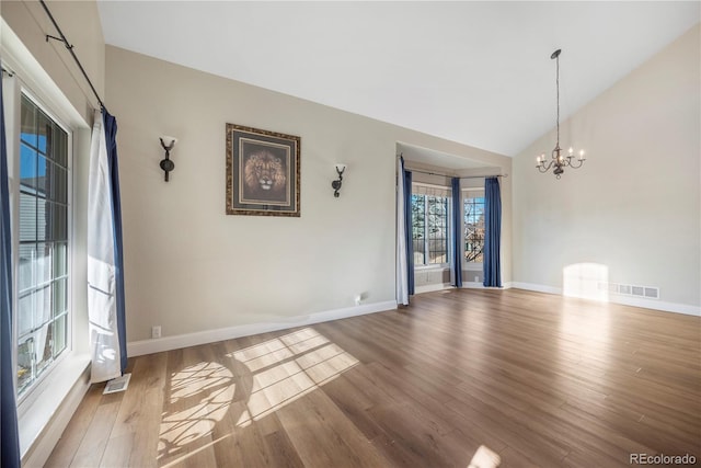 spare room featuring hardwood / wood-style floors, lofted ceiling, and an inviting chandelier