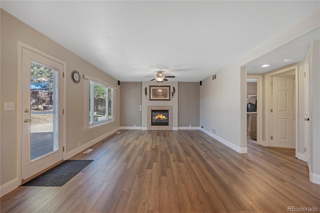 unfurnished living room with wood-type flooring, ceiling fan, and a tiled fireplace