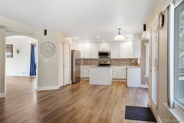 kitchen with white cabinets, appliances with stainless steel finishes, light wood-type flooring, and pendant lighting