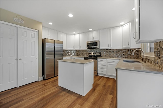 kitchen with appliances with stainless steel finishes, sink, hardwood / wood-style floors, a center island, and white cabinetry