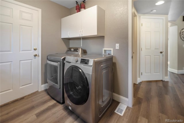 laundry area featuring cabinets, wood-type flooring, and separate washer and dryer